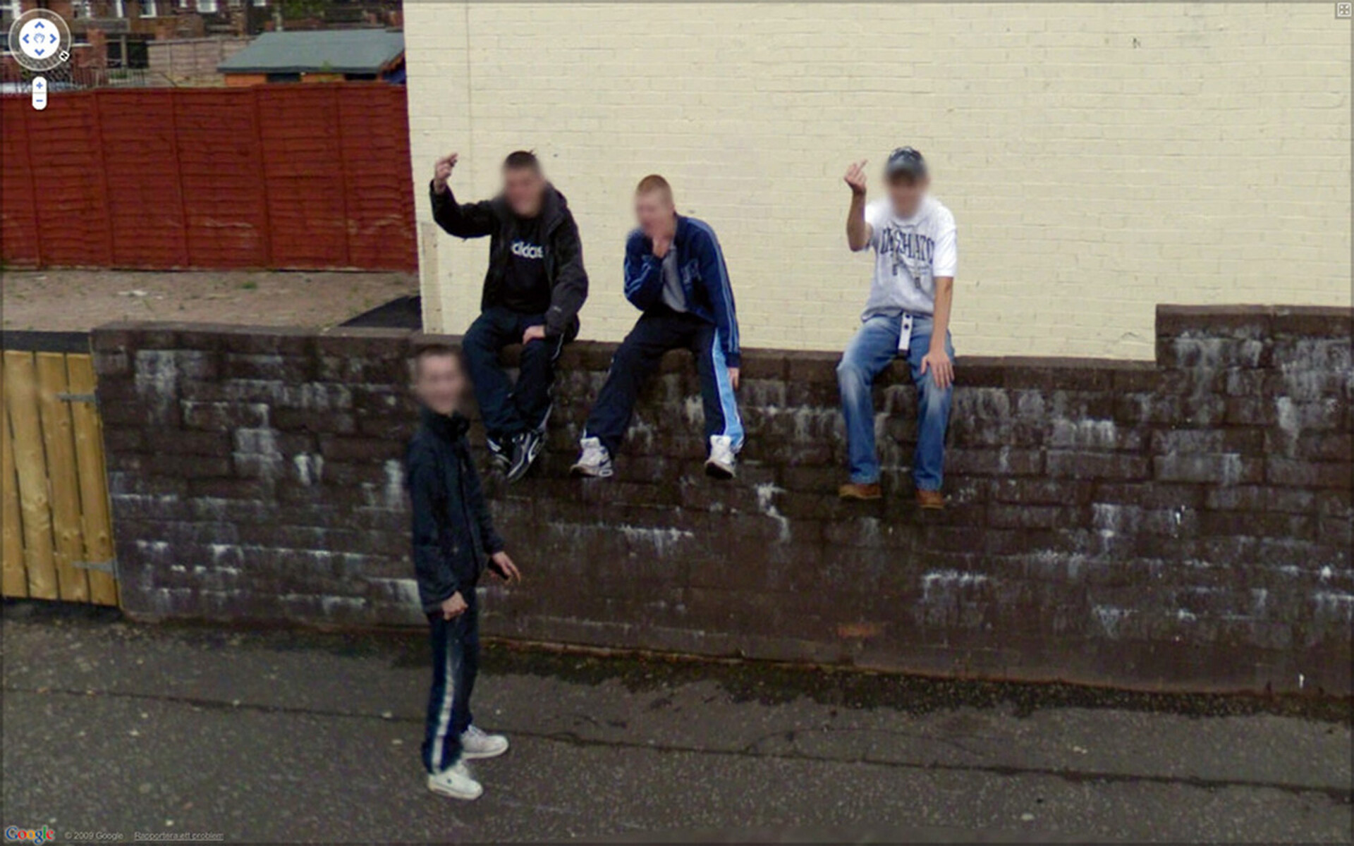  Zdjęcie z projektu 9 Eyes Johna Rafmana, w ramach którego artysta szukał ciekawych fotografii wykonanych przez aparaty Google Street View. Na tym zdjęciu widzimy brudny ceglany mur przy ulicy. Na murze siedzi trzech chłopaków w dresach. 
